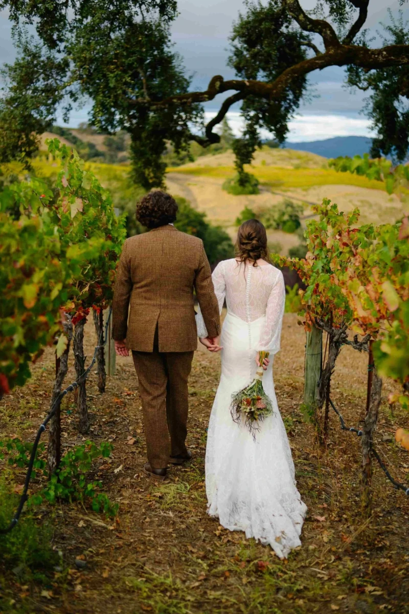 Bride and Groom walking away in vineyard with hills in the distance